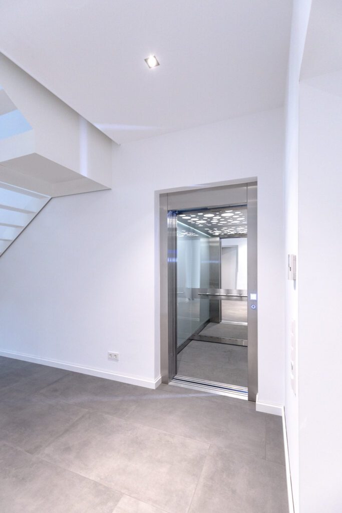 Huislift met glazen deuren en verlichte cabine in een witte hal