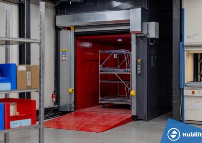 Goederenlift met open snelle roldeur en rolcontainer in de cabine bij Veth Propulsion