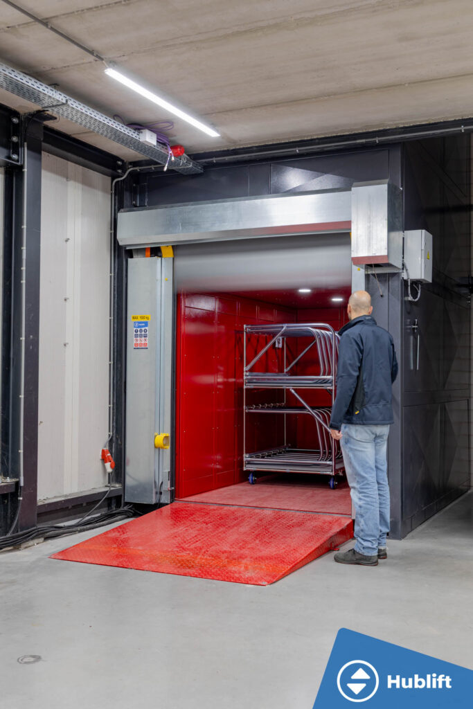 Open goods lift with red car and control panel next to the shaft door