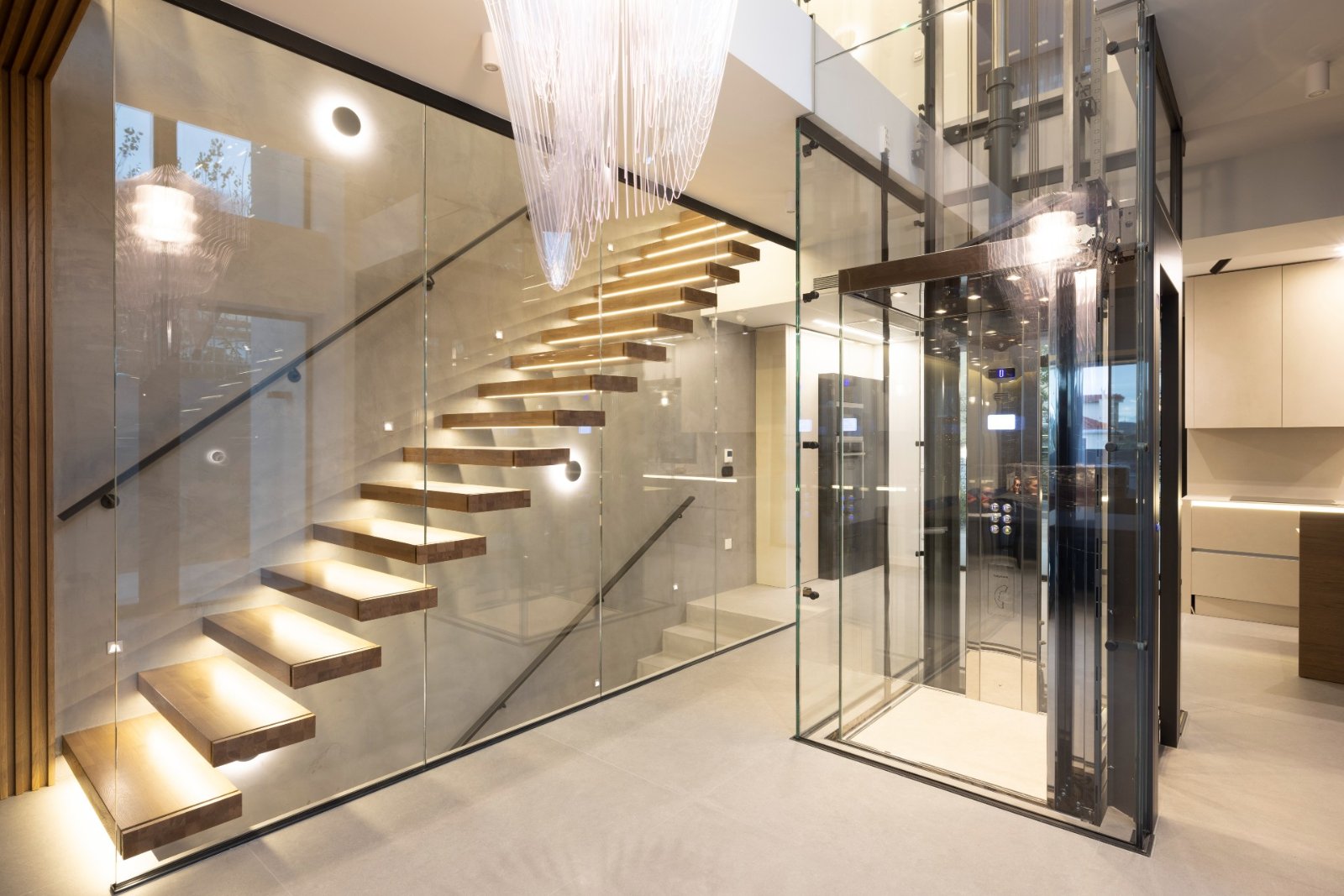 Home lift with a glass shaft next to a floating staircase in a modern house