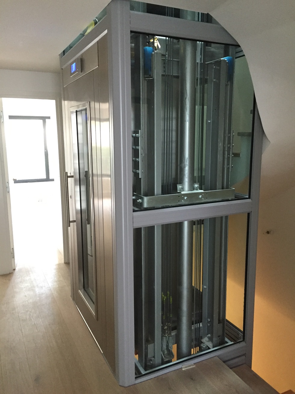 Home lift with a glass shaft and grey frame in a living room