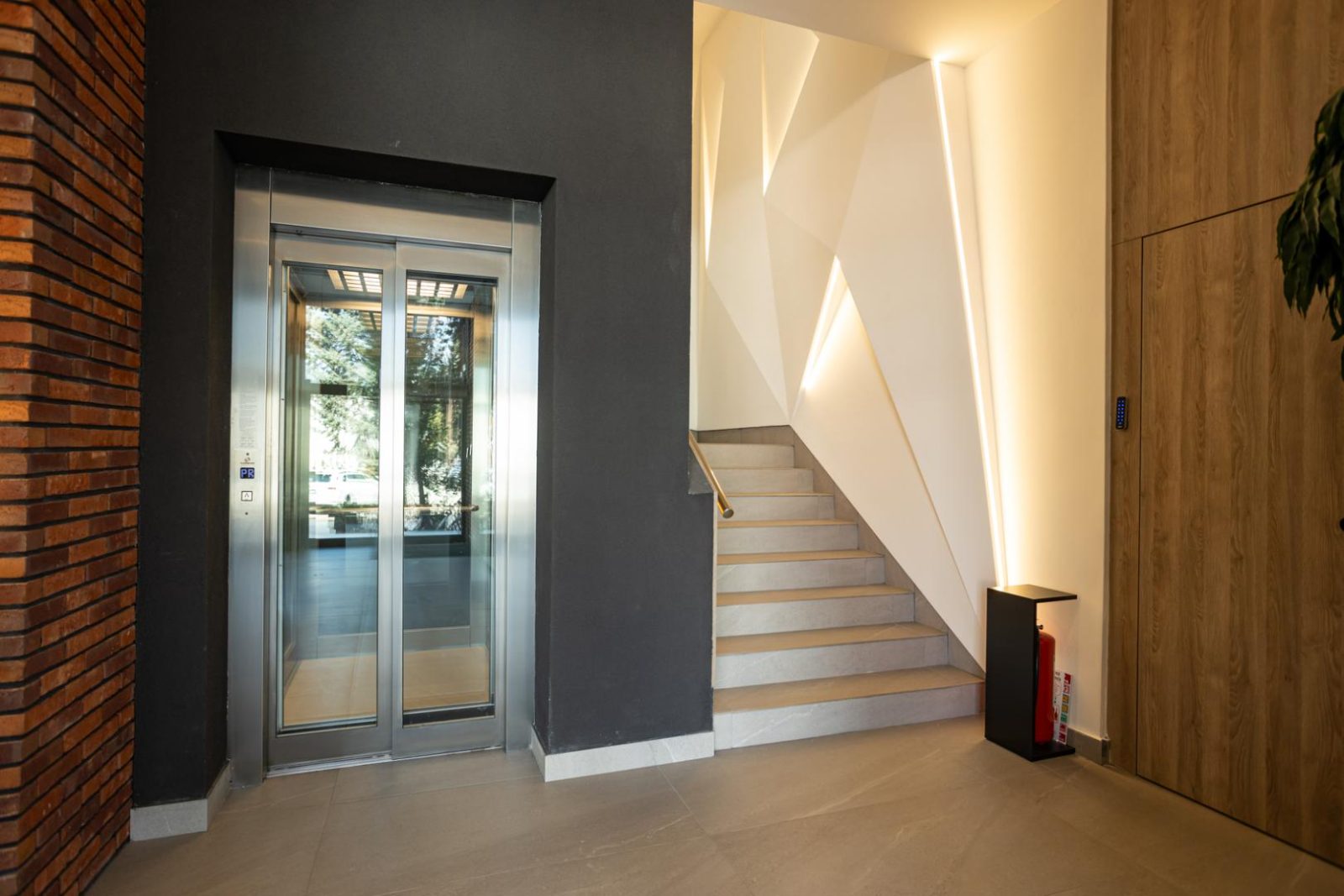 Personenlift met glazen deuren in een entree met houten wand en trap