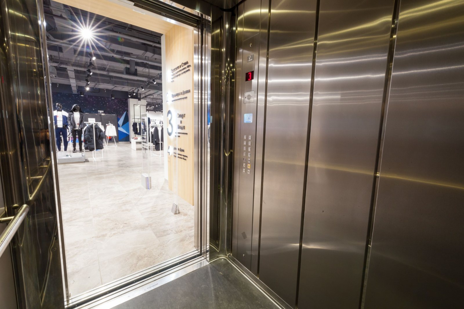 Open RVS personenliftcabine met zicht op een winkel